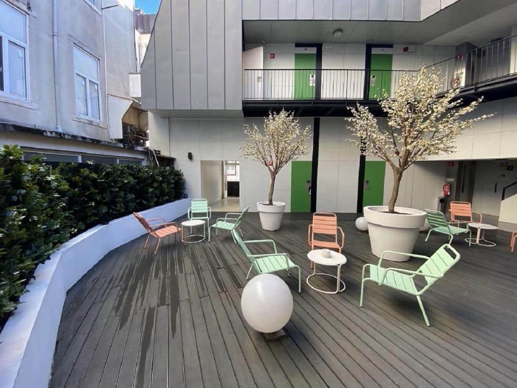 Terraço comum do Hotel Gat Rossio com vasos de plantas, pequenas mesas com cadeiras coloridas e chão em deck de madeira, nas traseiras do edifício.