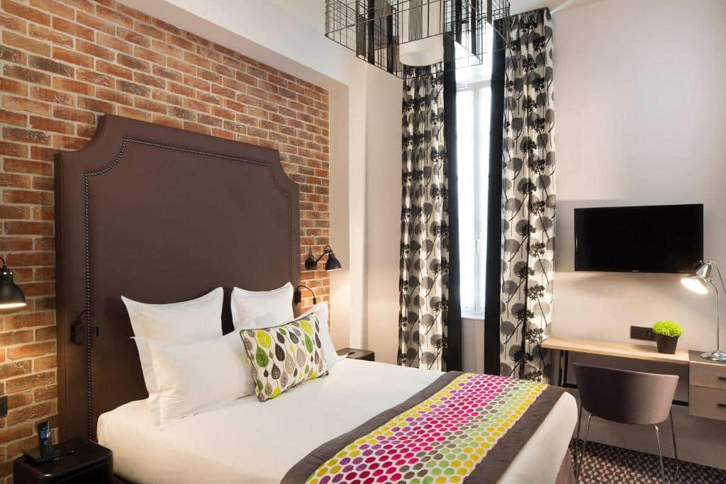 Quarto do Hôtel Fabric com cama, parede de tijolo, secretária e cortinas estampadas.