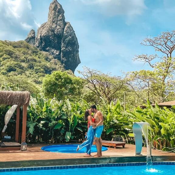 Casal a beijar-se em frente à piscina de um hotel em Fernando de Noronha, com vista para o morro do pico