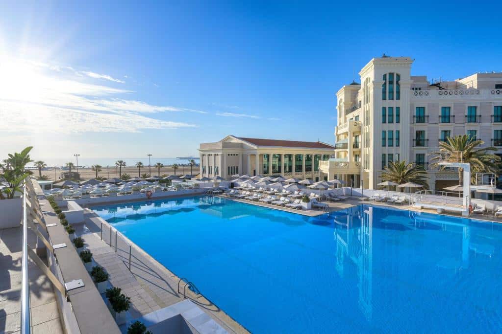 Resort luxuoso do Las Arenas Balneario Resort, com piscina azul-turquesa e espreguiçadeiras brancas à beira-mar num dia soalheiro.