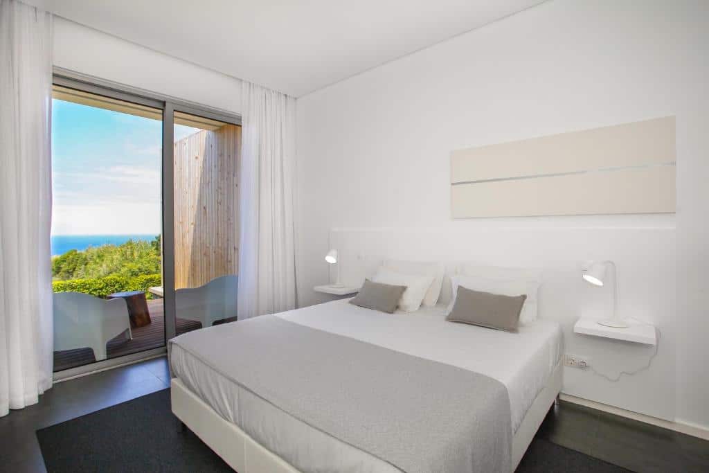 Quarto do Mosteiros Place, com cama de casal e portas de vidro com acesso à varanda.