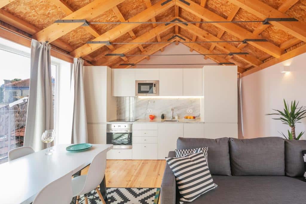 Sala de estar do Indulge Porto Flats, com sofá à direita, uma mesa com cadeiras à esquerda e, ao fundo, armários com fogão e micro-ondas.