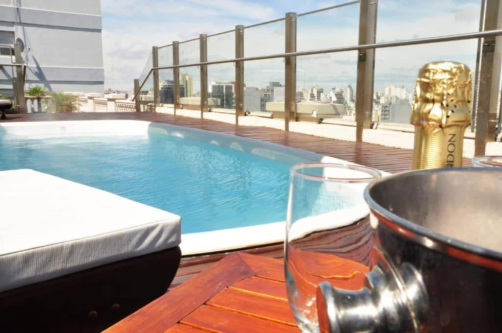 área da piscina no terraço do Scala Hotel Buenos Aires, com deck de madeira, vista panorâmica da cidade e uma mesa com champanhe e copos, num ambiente sofisticado