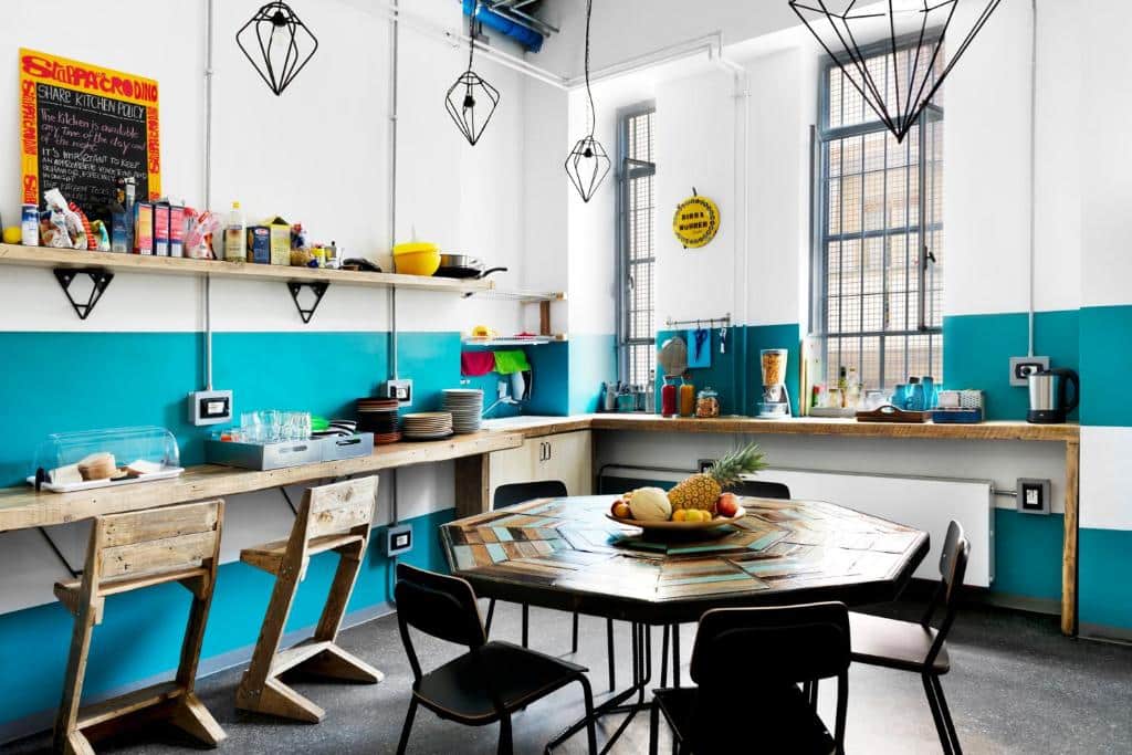 Espaço de refeições do Madama Hostel &amp; Bistrot com uma mesa de cinco lugares e bancadas com loiça e copos, num ambiente rústico e bem equipado