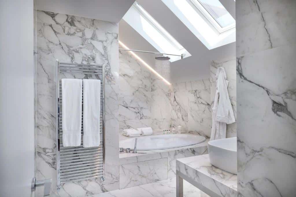 Casa de banho em mármore do Magna Pars l'Hotel à Parfum, com janelas em ângulo de 90 graus voltadas para uma banheira oval, roupões e toalhas brancas pendurados