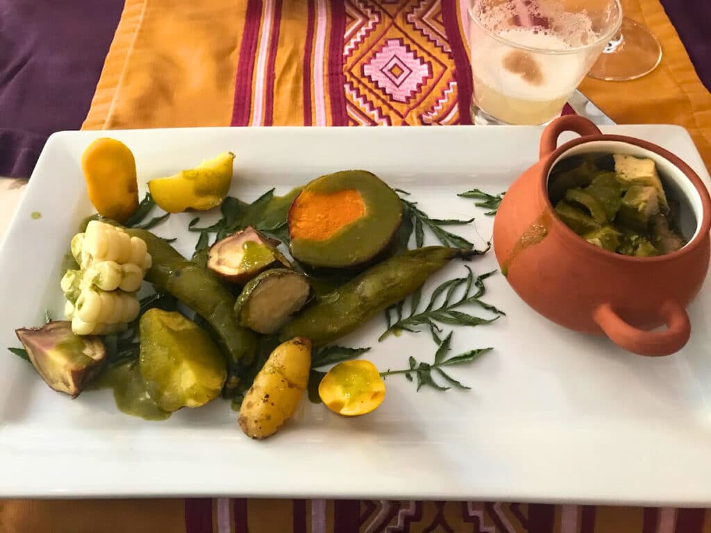 Prato de Pachamanca com vários tipos de batata e milho, ao lado de uma taça de barro com pão
