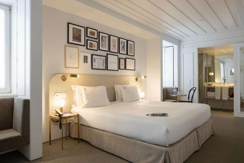 Quarto do Lisboa Pessoa Hotel com uma cama de casal, vários quadros na parede de trás, mesas de cabeceira com candeeiros e duas janelas.