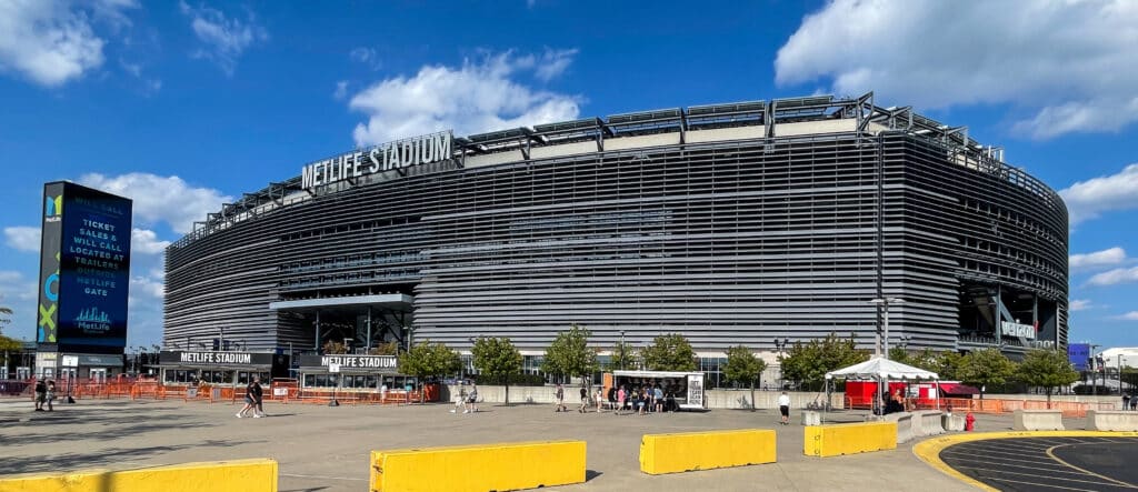 Estádio MetLife, um grande complexo desportivo com fachada em estrutura metálica preta, em tempo soalheiro, com céu azul e nuvens.
