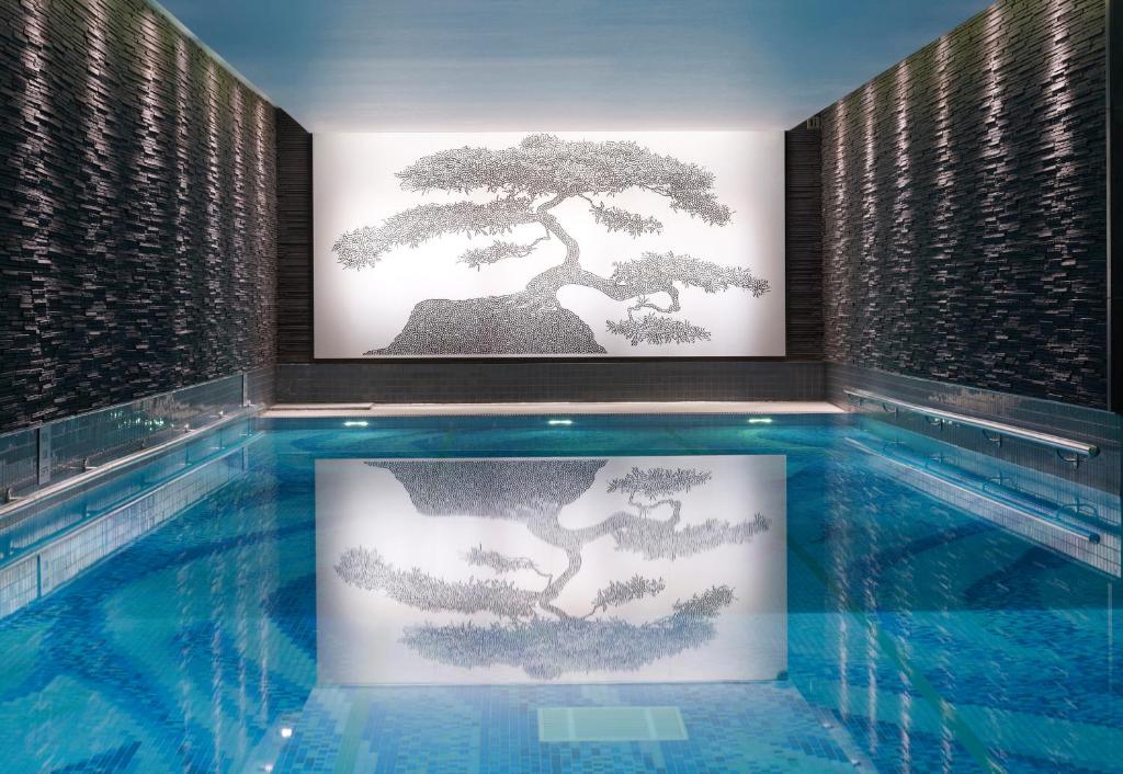 Piscina coberta do The Langham London com paredes em pedra preta e um mosaico na parede em frente, refletido na água.