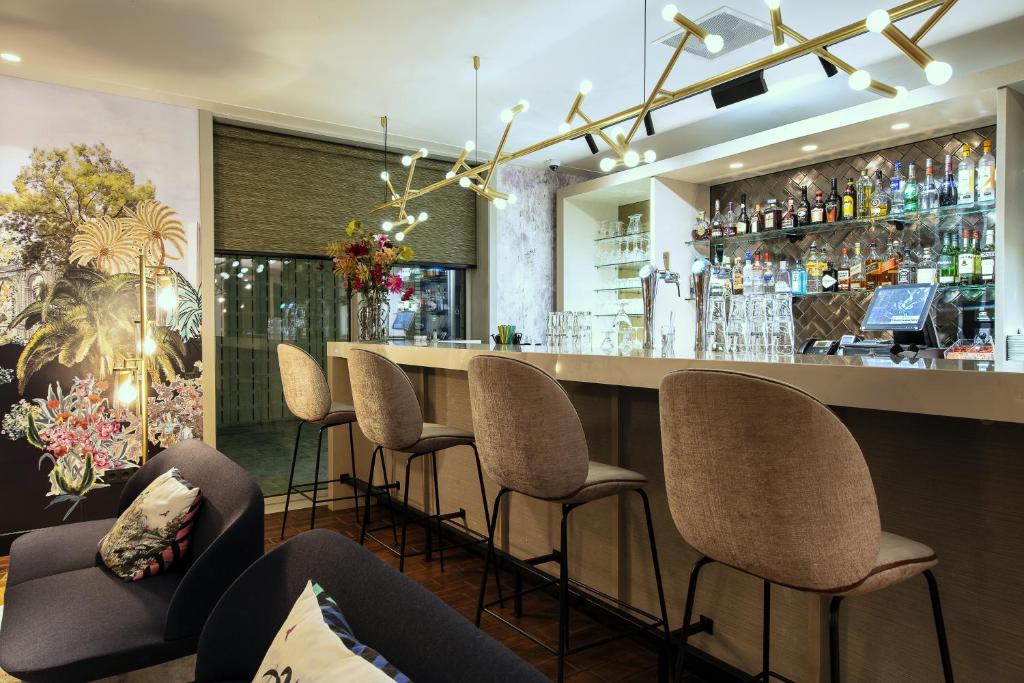 Zona de bar moderna do Monet Garden Hotel, com bancos altos bege, um bar bem fornecido e retroiluminado e candeeiros contemporâneos no topo.