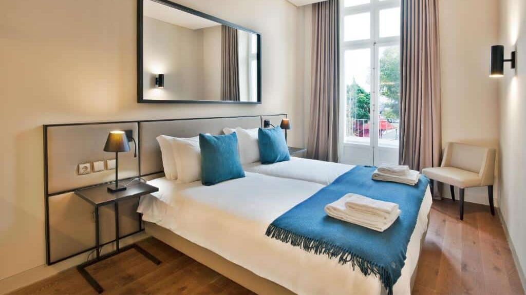 Quarto do Lisbon Five Stars Apartments 8 Building com cama de casal, almofadas azuis, mesas de cabeceira, um espelho grande e uma janela com cortinas que deixam entrar luz natural.