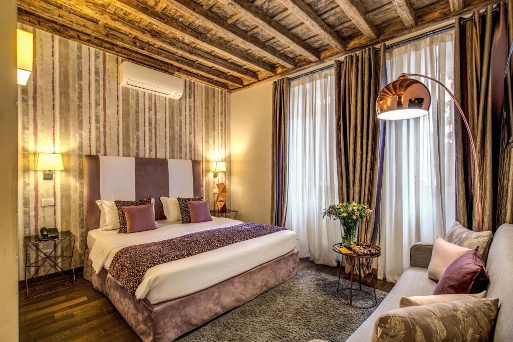 quarto do Trevi Beau Boutique Hotel, com cama de casal grande com pormenores em madeira e lilás, janelas grandes com cortinas, um sofá em frente, mesa e candeeiro de cada lado e ar condicionado, tudo muito detalhado