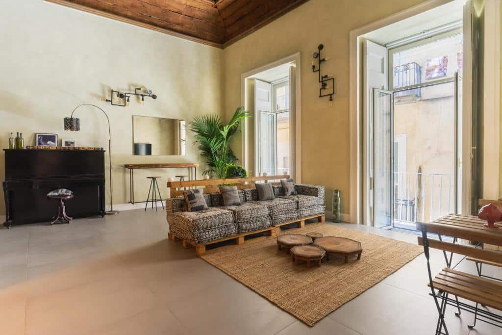 Sala de estar acolhedora com móveis rústicos, incluindo sofá de paletes e bancos de madeira, objetos decorativos e uma janela panorâmica com vista para o exterior, no Hospetel Secret Garden Napoli.