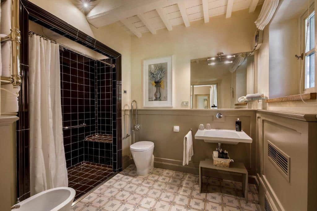 Casa de banho do quarto duplo do Borgo Del Cabreo, um dos hotéis na Toscana, com sanita, bidé, lavatório, bastante espaço entre os elementos e zona de duche separada, com barra de apoio e assento para cadeiras de rodas