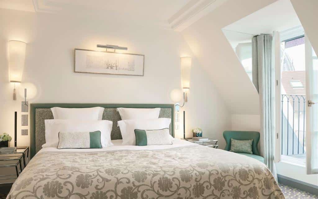 A imagem mostra um quarto do Le Burgundy Paris, com cama bem feita e roupa de cama estampada num quarto bem iluminado, duas mesas de cabeceira, uma poltrona e uma porta para uma pequena varanda.