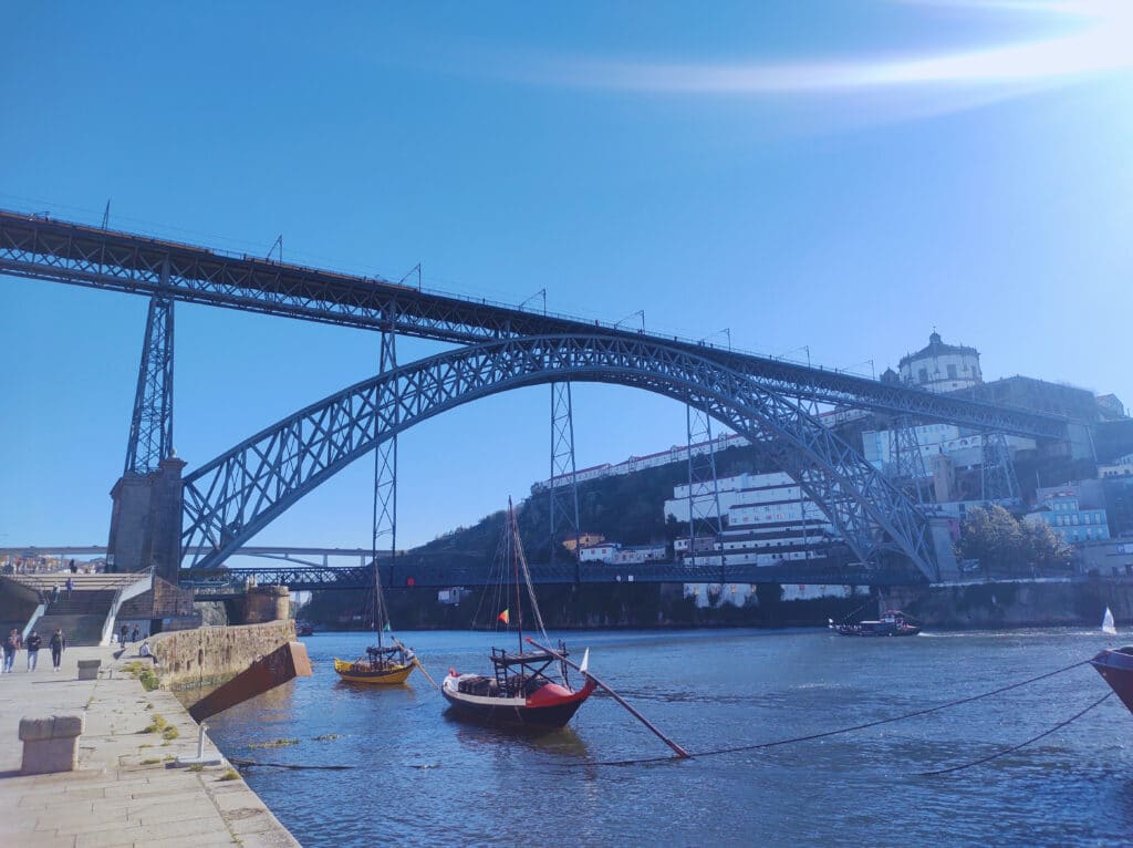 Ponte D. Luís I durante o dia, com barcos no rio à direita e a ponte ao fundo.