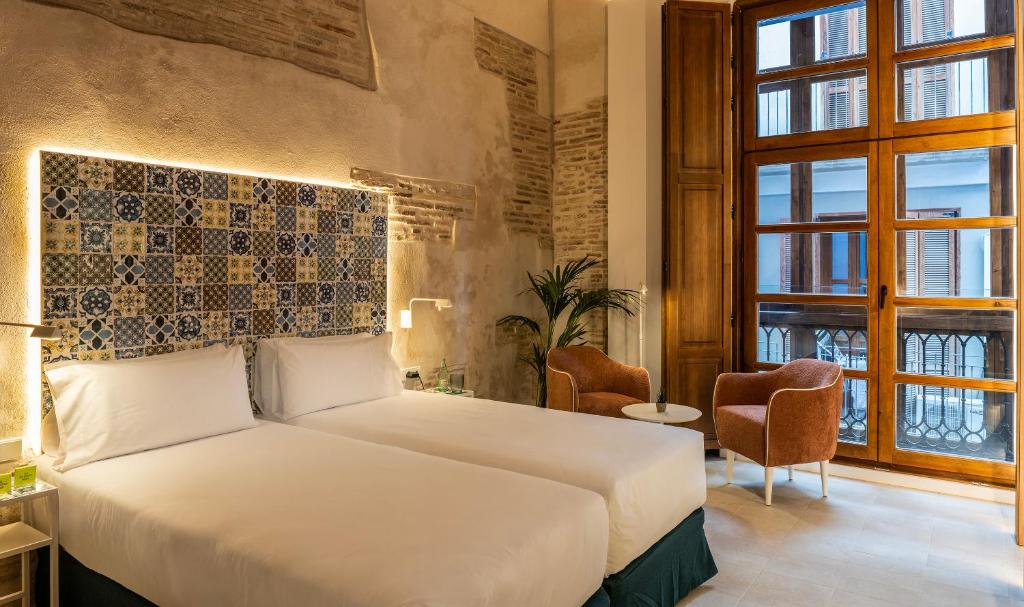 Quarto do Axel Hotel Valencia com paredes de tijolo à vista, cama de casal com cabeceira decorada e janela ampla com vista para a cidade.