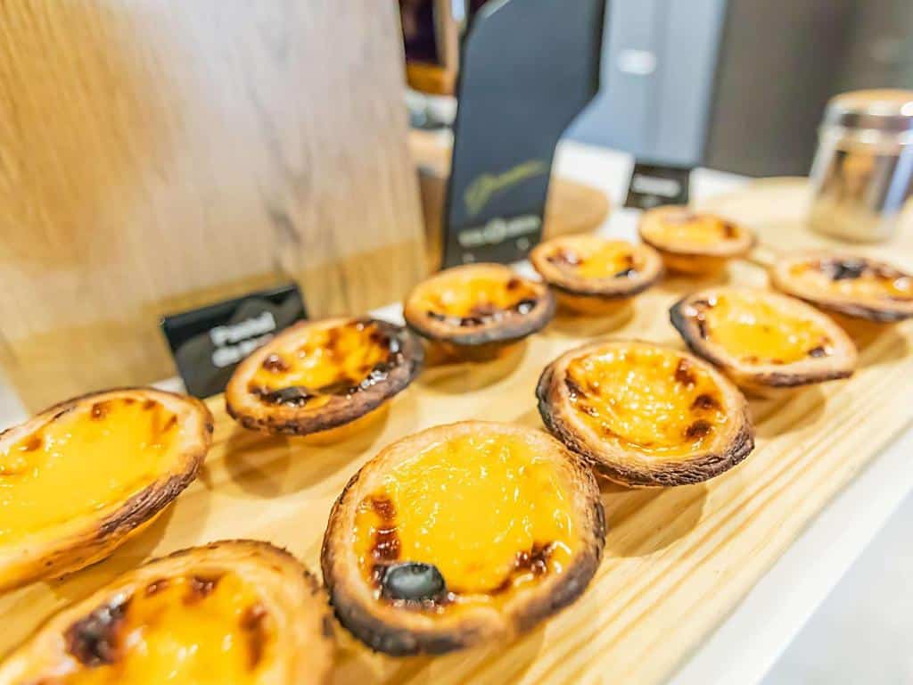 Fila de pastéis de nata com bordos ligeiramente dourados, dispostos numa tábua de madeira.