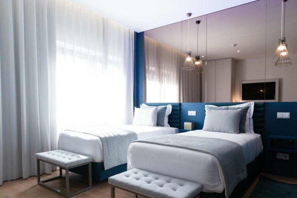 Quarto moderno no Zurin Charm Hotel com duas camas de solteiro, bancos cinzentos aos pés, candeeiros suspensos e grandes janelas com cortinados transparentes.