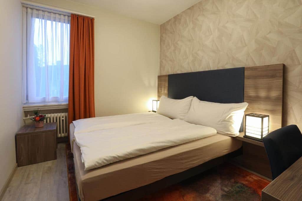 Quarto do Hotel Spatz, em Lucerna, com cama de casal e janela com cortinas vermelhas.