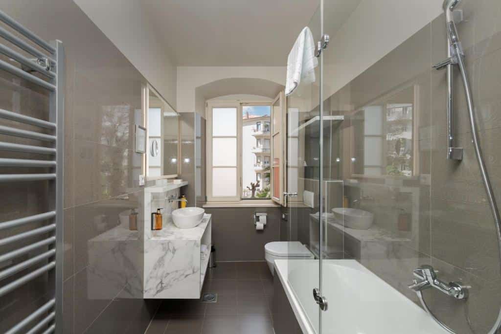 Casa de banho moderna com cabina de vidro, lavatório com bancada de mármore e toalheiro cromado, no Bastion Heritage Hotel