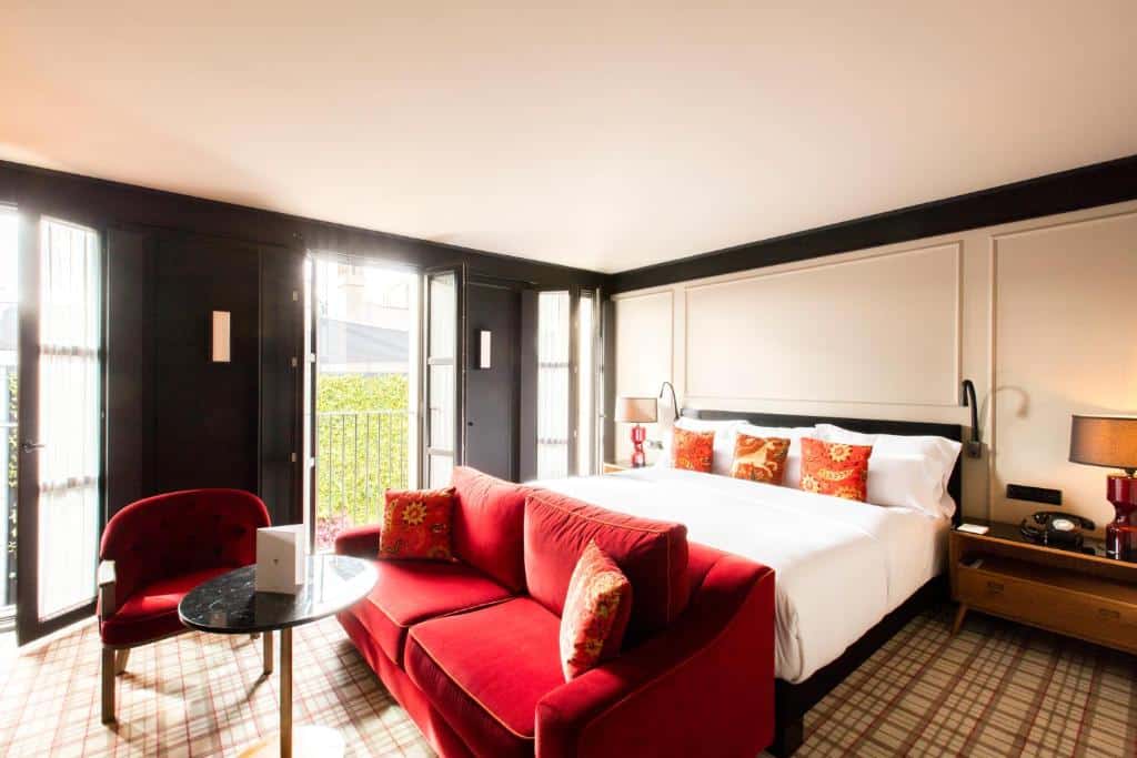 Quarto do Wittmore Hotel, uma das recomendações de hotéis no Bairro Gótico em Barcelona. A cama de casal tem mesas de cabeceira de ambos os lados, uma zona de estar com sofá e cadeirão aos pés e três janelas abertas.