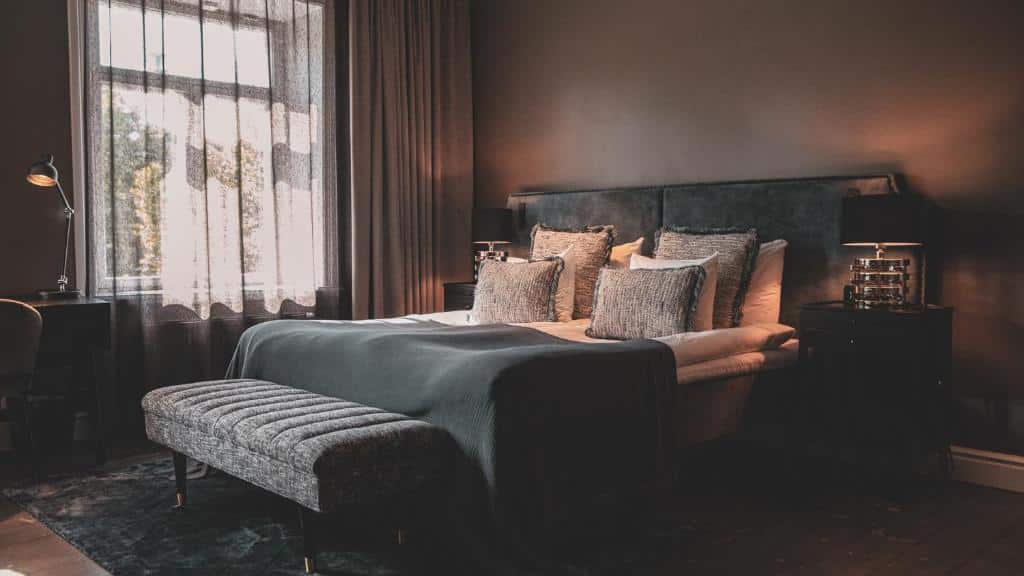 Quarto do Backstage Hotel Stockholm com cama de casal, cómodas com candeeiros e um banco estofado.