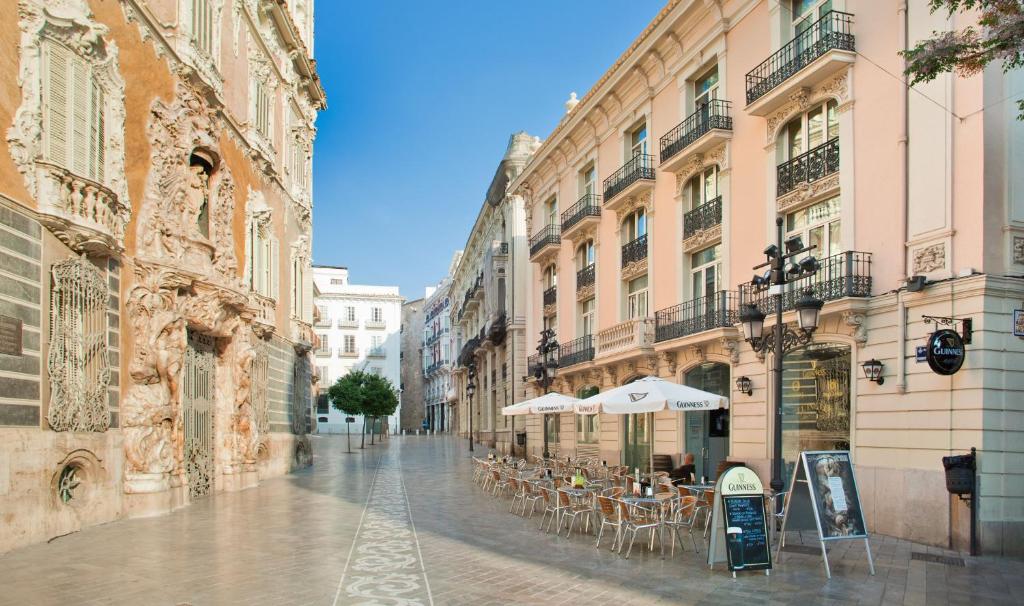Praça soalheira com edifícios históricos, varandas e fachadas decoradas, mesas de café com guarda-sóis e pessoas a comer ao ar livre, junto ao SH Ingles Boutique Hotel.