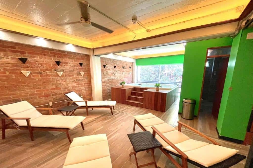 Uma sala de relaxamento do Joint Boutique Hotel com espreguiçadeiras, um jacúzi, paredes de tijolo, detalhes em verde e grandes janelas com luz natural.