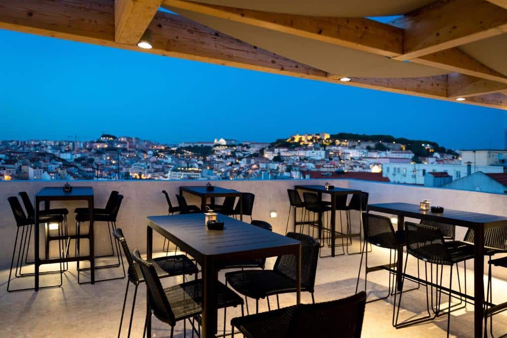 Terraço do Lisboa Pessoa Hotel com vista para a cidade, com mesas e cadeiras pretas e alguns pontos de iluminação indireta.
