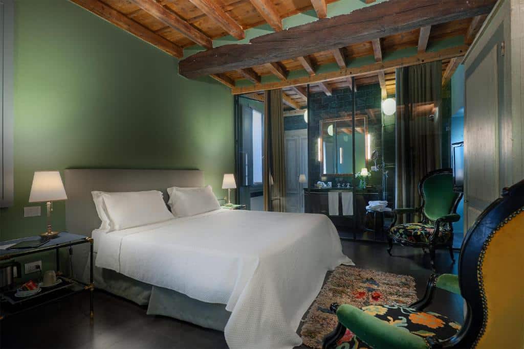Quarto do Maison Borella com cama de casal, duas poltronas verdes, tapete florido, toucador e um amplo espelho, decorado em tons de verde e branco