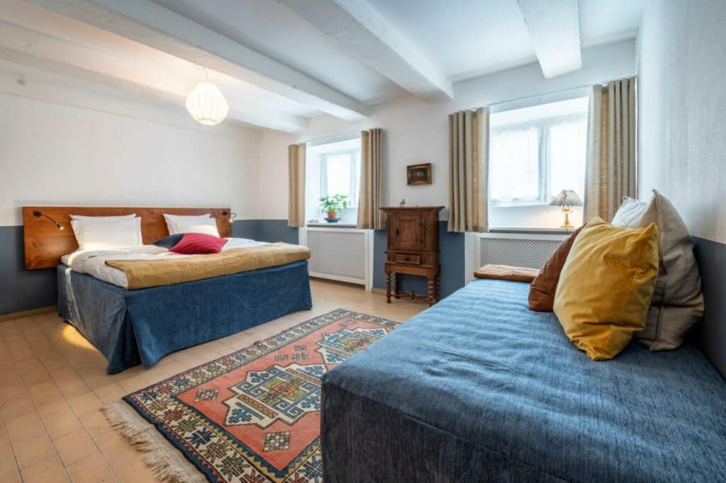 Quarto espaçoso do hotel Kanalhuset com duas camas, uma de casal e outra de solteiro. Tem também duas janelas e um pequeno armário.