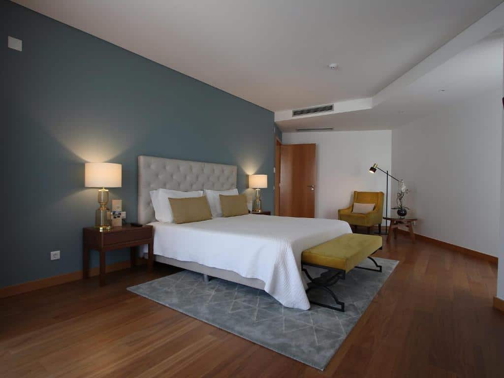Quarto moderno no Consolata Hotel com uma cama de casal, candeeiros, banco e cadeira amarelos, pavimento de madeira e parede de destaque azul, para representar onde ficar em Fátima.