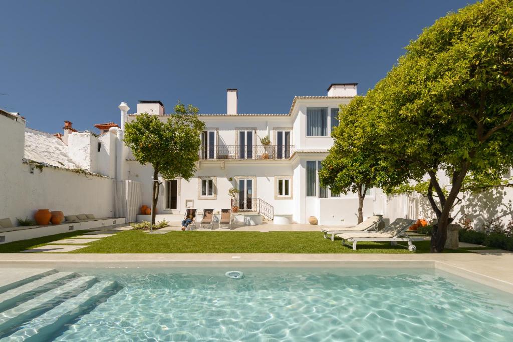 Piscina do Dona Graca Lisbon Apartments com um jardim em redor e algumas árvores, além de espreguiçadeiras brancas