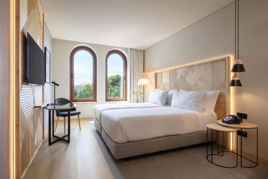 Quarto moderno do INNSiDE by Meliá Braga Centro, com cama grande, TV de parede, secretária, janelas redondas e mesas de cabeceira com candeeiros.