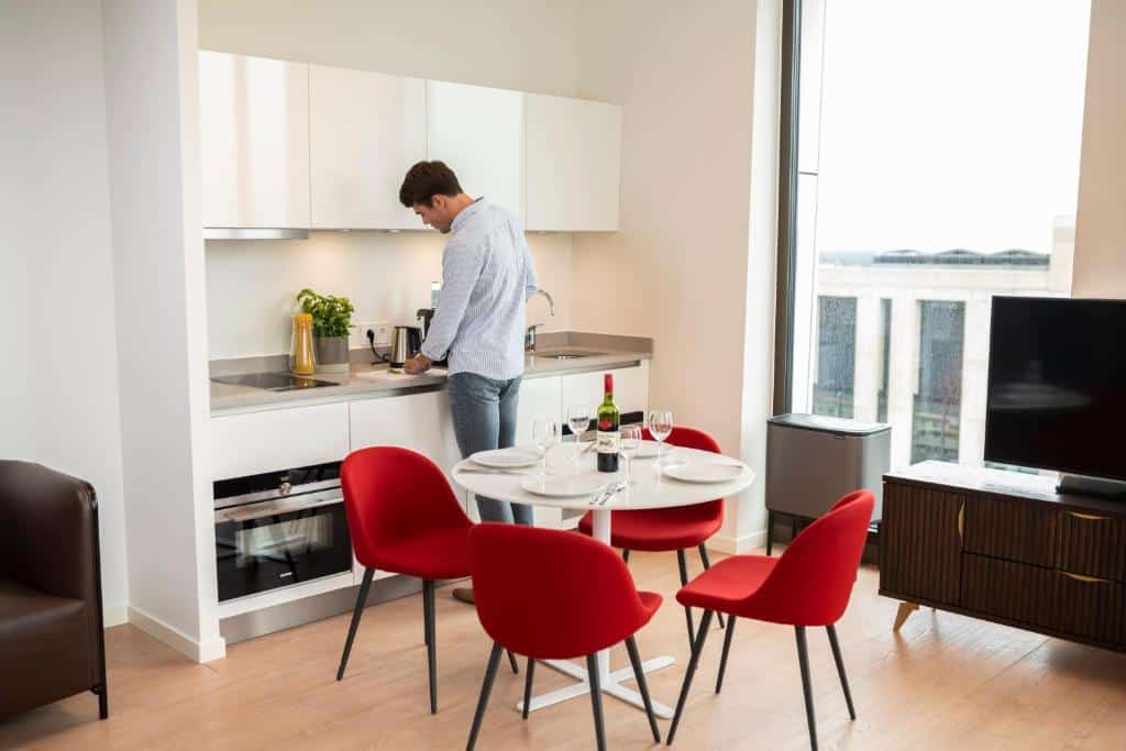 Cozinha de um dos estúdios do Premier Suites, com mesa redonda e quatro cadeiras vermelhas, e um balcão com lavatório, forno e armário suspenso
