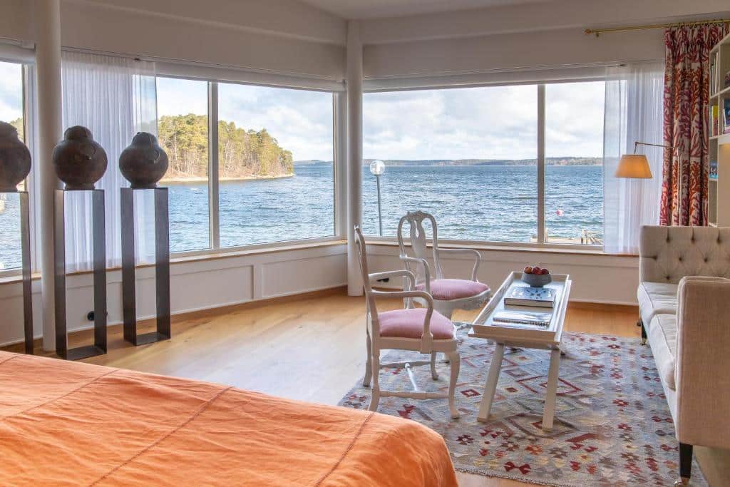 Quarto do Vår Gård Saltsjöbaden com cama de casal com vista para o mar, sofá e cadeiras.