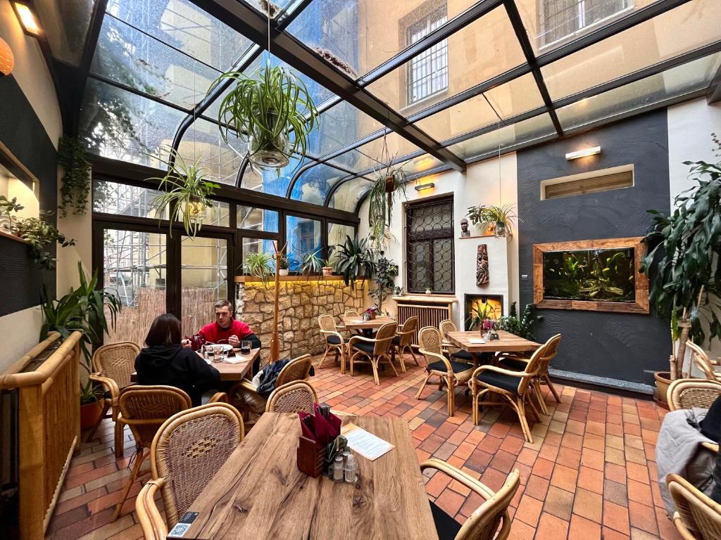 Cafetaria com teto de vidro da Pension Sklep, com cadeiras de vime, vasos de plantas, um aquário e pessoas sentadas às mesas.