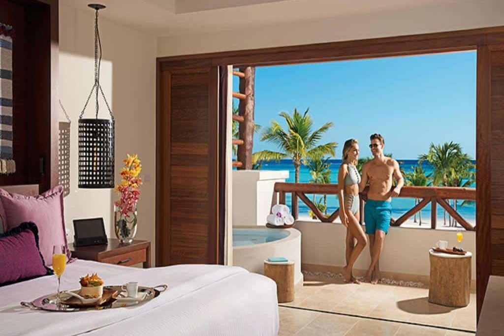 Casal em suíte de hotel com vista para praia paradisíaca e hidromassagem externa