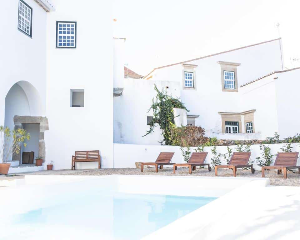 Piscina em frente a casa branca com espreguiçadeiras de madeira na A Burguesa - Guesthouse, em Castelo de Vide