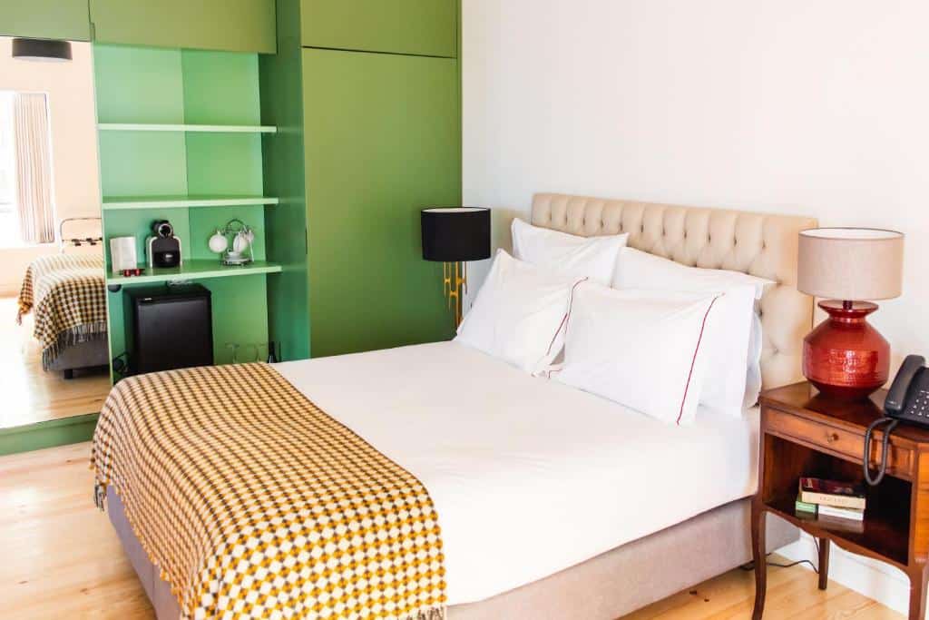 Cama bem arrumada com almofadas brancas, prateleiras verdes e uma mesa de cabeceira com candeeiro e telefone, num quarto do Monte Belvedere Hotel by Shiadu.
