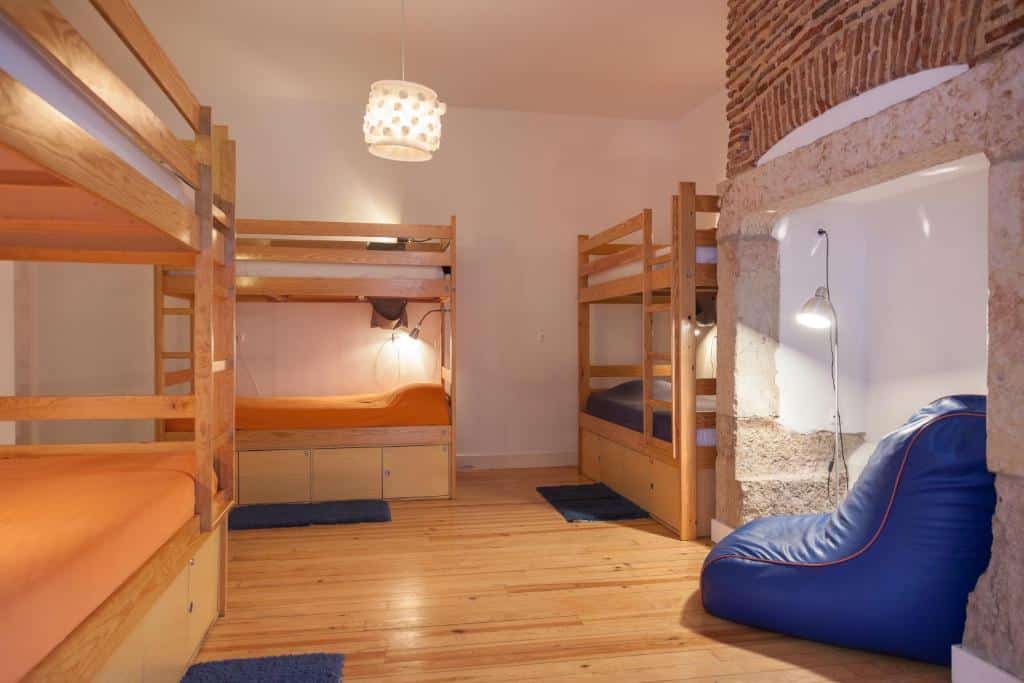 Quarto partilhado do Lisbon Lounge Hostel com três beliches, um candeeiro de teto e uma pufe grande junto de um candeeiro de pé