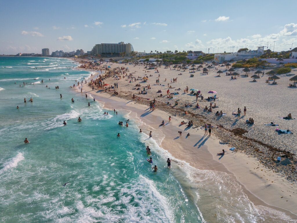 Playa Nizuc na Zona Hoteleira em Cancún, com orla extensa, longa faixa de areia e mar de água verde-clara, com muitas pessoas e alguns hotéis junto à praia