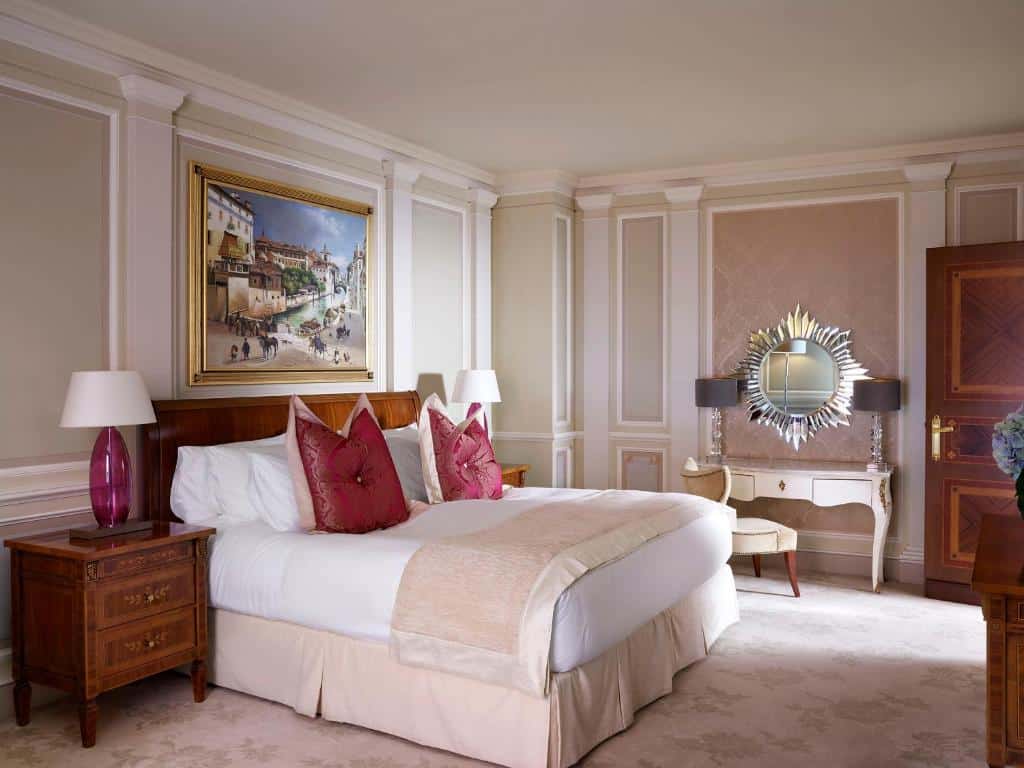 Quarto do Hotel Principe Di Savoia em estilo renascentista, em tons de branco e rosa-claro, com cama de casal, toucador com espelho redondo e dois móveis de cabeceira em madeira