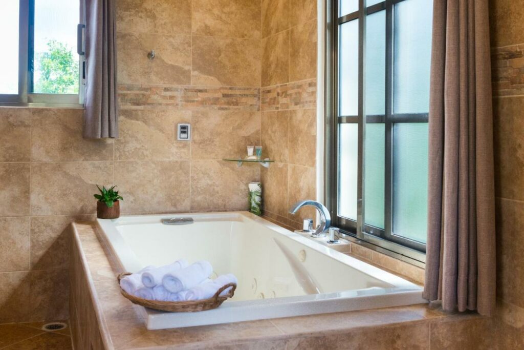 Banheira do Álamos Inn Hotel con Jacuzzi y Piscina com toalhas disponíveis, uma janela e um vaso de flores