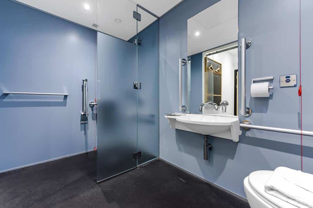 Casa de banho do The Z Hotel Trafalgar com box aberto, barras de apoio, cordão de emergência e lavatório sem suporte por baixo