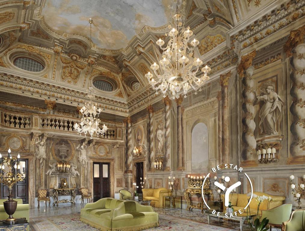 Interior do Grand Hotel Continental Siena, um dos hotéis na Toscana, com aspeto de castelo, pinturas nas paredes, lustres grandes, pinturas no teto, sofás e móveis de época