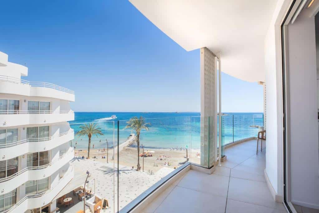 Varanda do One Ibiza Suites com vista para uma praia de areia, palmeiras e mar azul sob um céu limpo.