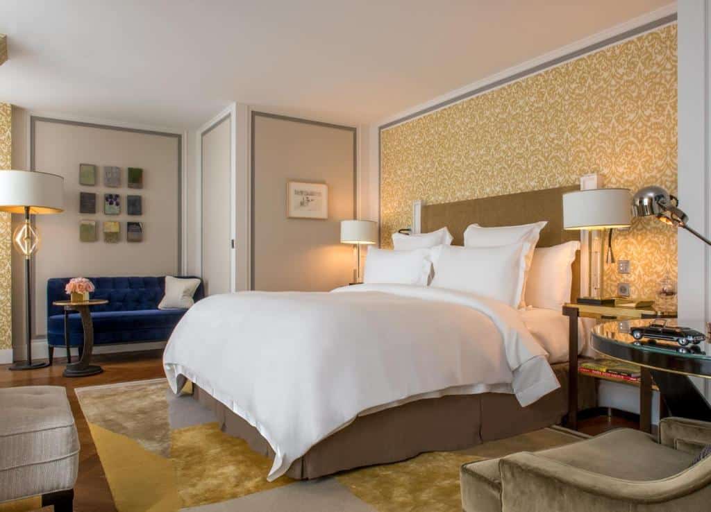 Um quarto do Hotel de Crillon com uma cama grande, parede de destaque com padrão amarelo, sofá azul e duas luminárias de cabeceira.