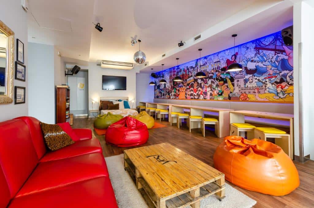Espaço comum do Yes Lisbon Hostel com sofás, móveis coloridos, pequenas mesas de madeira com bancos e um mural desenhado